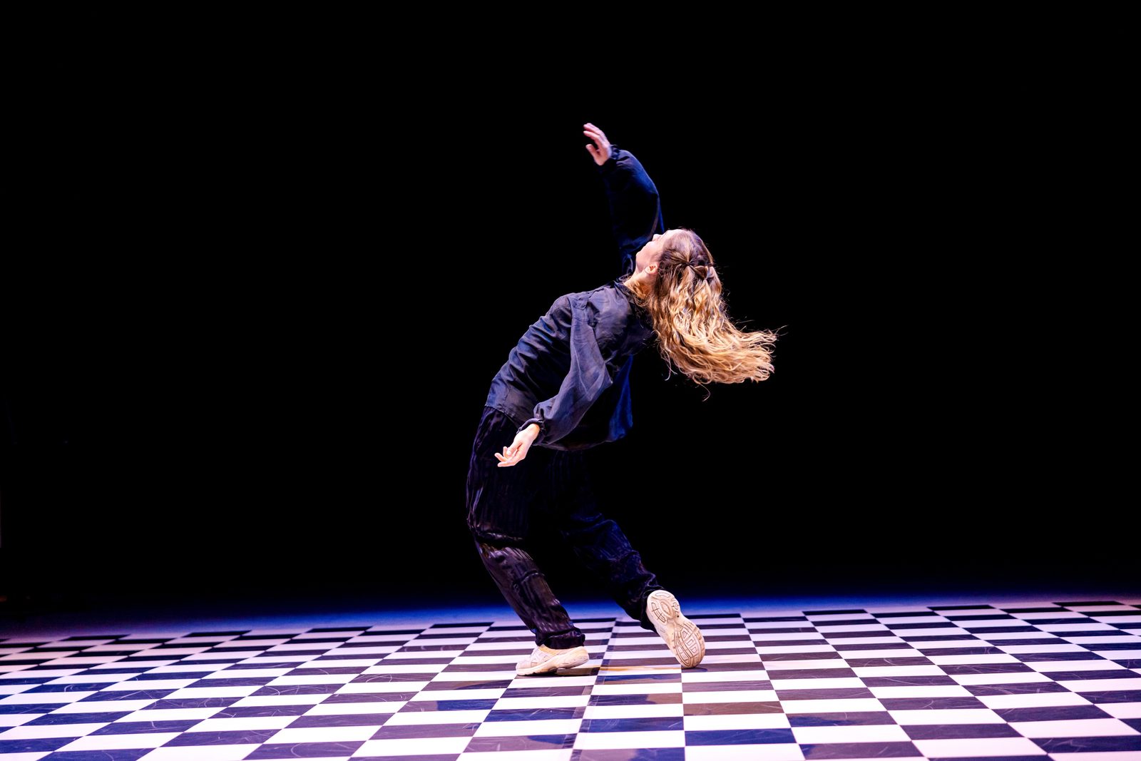 A dancer of GROOVE in a dynamic backward motion on the checkered stage floor