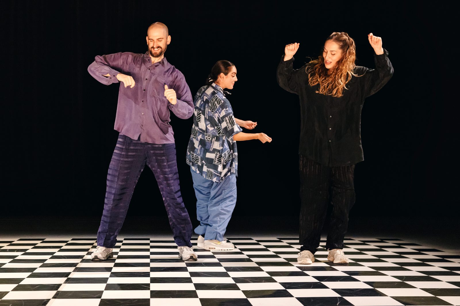 Three dancers of GROOVE in motion on the stage's checkered floor